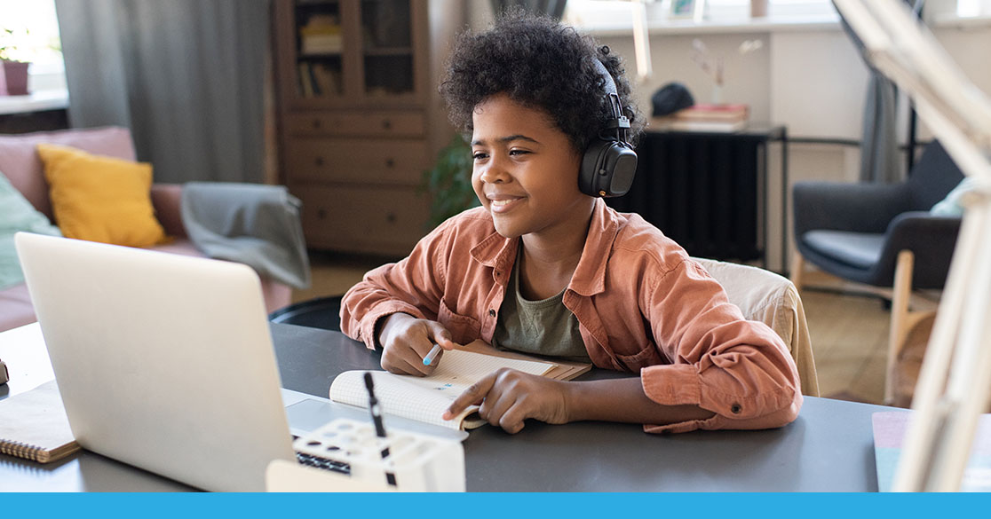 Student participating in Florida Virtual School online learning, using a laptop and headphones while taking notes at a home study space.